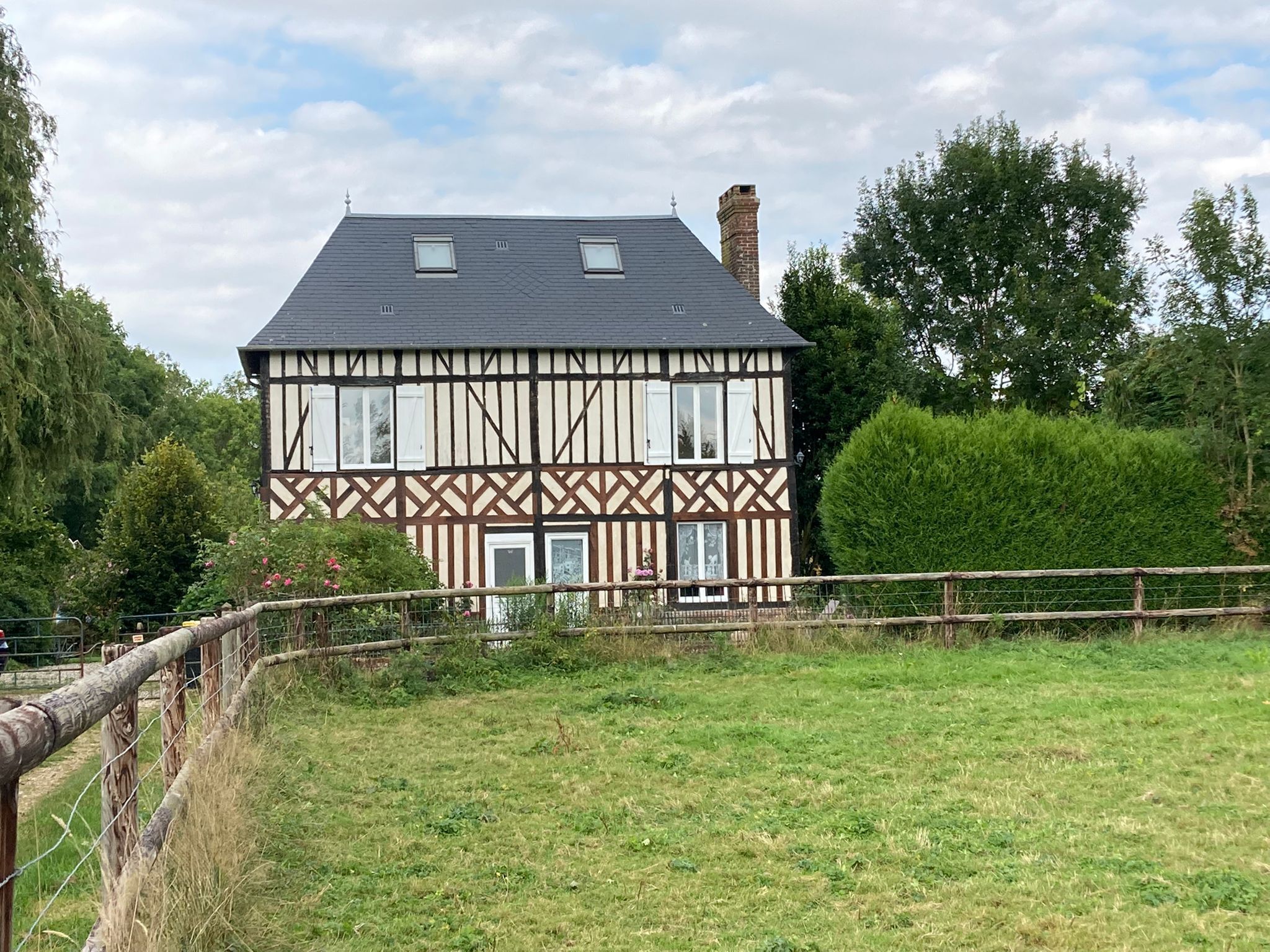 Une maison de style Tudor à deux étages, dotée d’un toit à forte pente, de lucarnes et d’une cheminée bien visible.