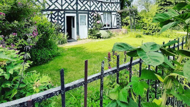 Una casa in stile Tudor con facciata simmetrica, ingresso centrale e un giardino curato con diverse piante e un recinto in legno.