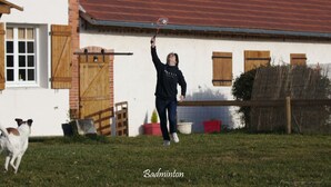 A person playing badminton in a backyard with a house in the background.