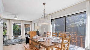 A dining area with a wooden table set for six, surrounded by wooden chairs, a chandelier, and a view of a backyard through large sliding doors. - Newly Renovated Luxury Villa- 5 minute walk to Beach! (Hilton Head Island)