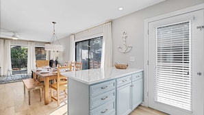 A modern kitchen with a marble countertop, light blue cabinetry, and a dining area with wooden furniture. - Newly Renovated Luxury Villa- 5 minute walk to Beach! (Hilton Head Island)