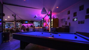 Une table de billard dans une pièce à la lumière tamisée, avec un bar en arrière-plan.