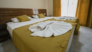 Deux lits avec des draps blancs et une couette jaune, une tête de lit en bois et une fenêtre avec des rideaux.