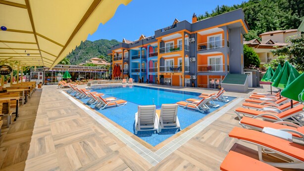 Une piscine avec des chaises longues, un espace de détente couvert et un bâtiment doté de balcons.