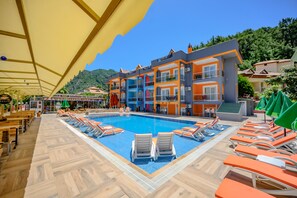 Une piscine avec des chaises longues, un espace de détente couvert et un bâtiment doté de balcons.