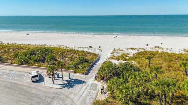 Vista aérea de una playa con un estacionamiento, una carretera y un sendero peatonal que conduce a la playa.