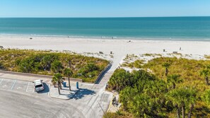 An aerial view of a beach with a parking lot, a road, and a pedestrian path leading to the beach.