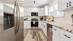Una cocina moderna con electrodomésticos de acero inoxidable, armarios blancos y piso de madera.
