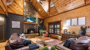 L’intérieur chaleureux d’un chalet en bois, avec une cheminée en pierre, des canapés en cuir, un téléviseur et des œuvres d’art encadrées.