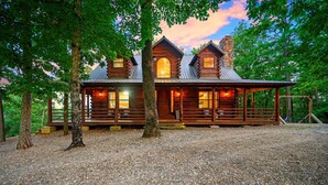 Une cabane en rondins dotée d’une véranda, de grandes fenêtres et d’une cheminée en pierre.