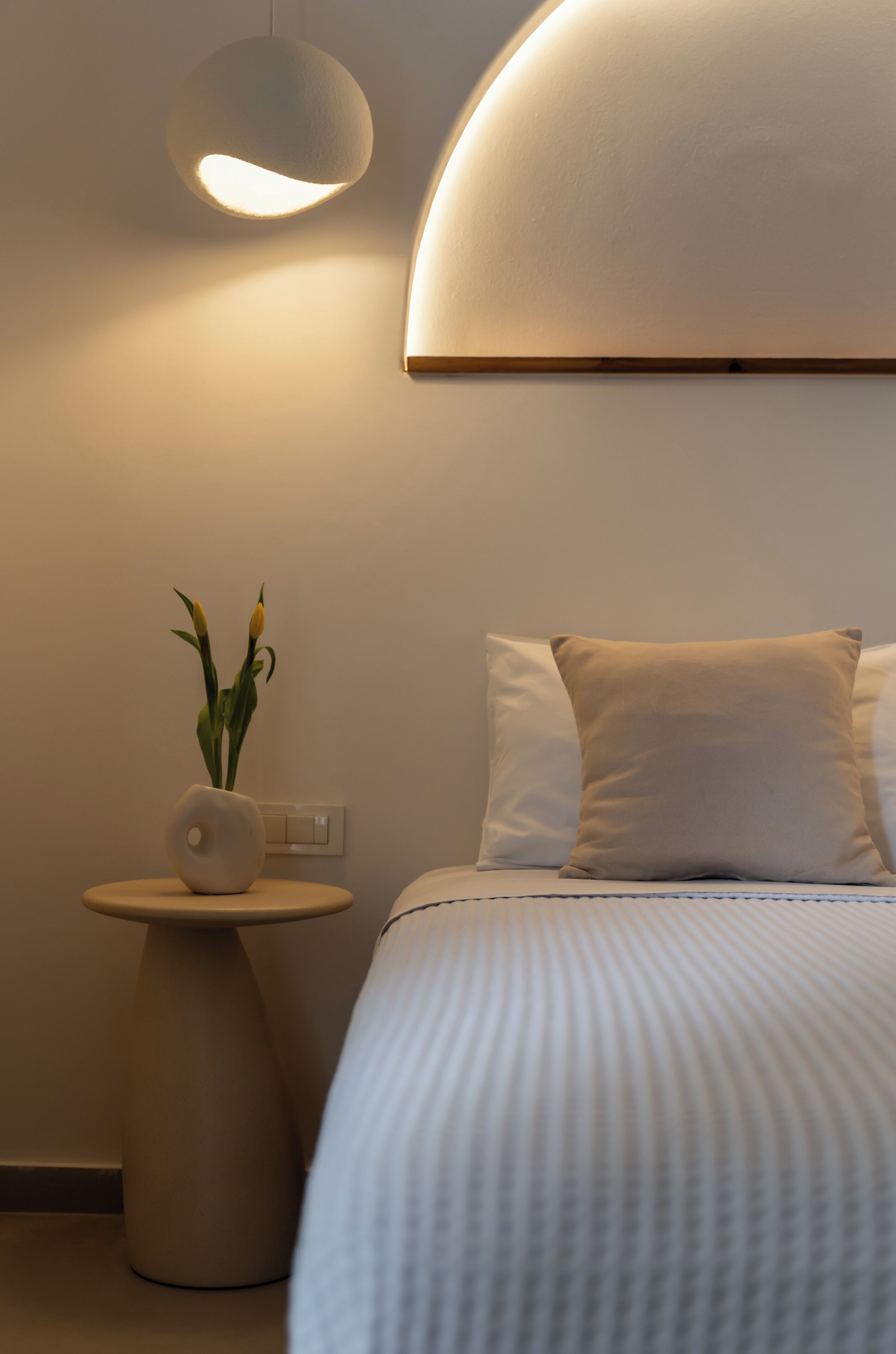 Una camera da letto moderna con un letto, un comodino con un vaso e una lampada a sospensione.