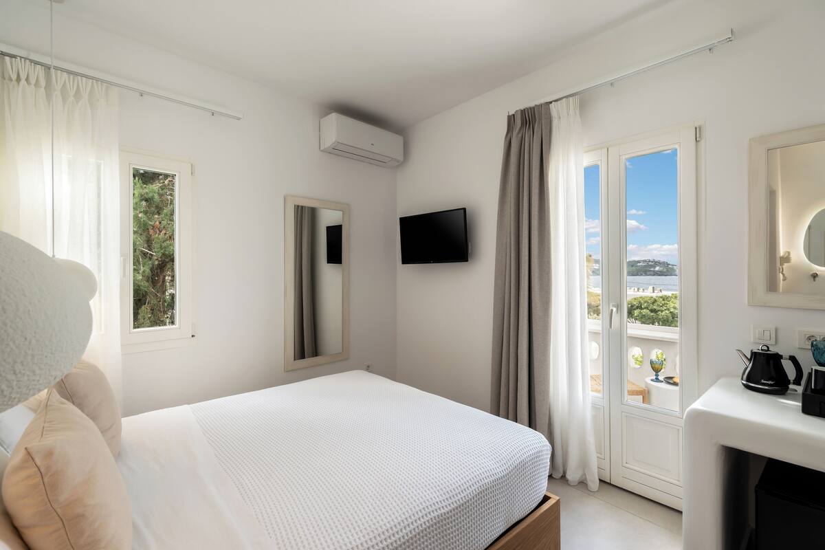 A bedroom with a bed, a TV, a window, and a balcony with a view.