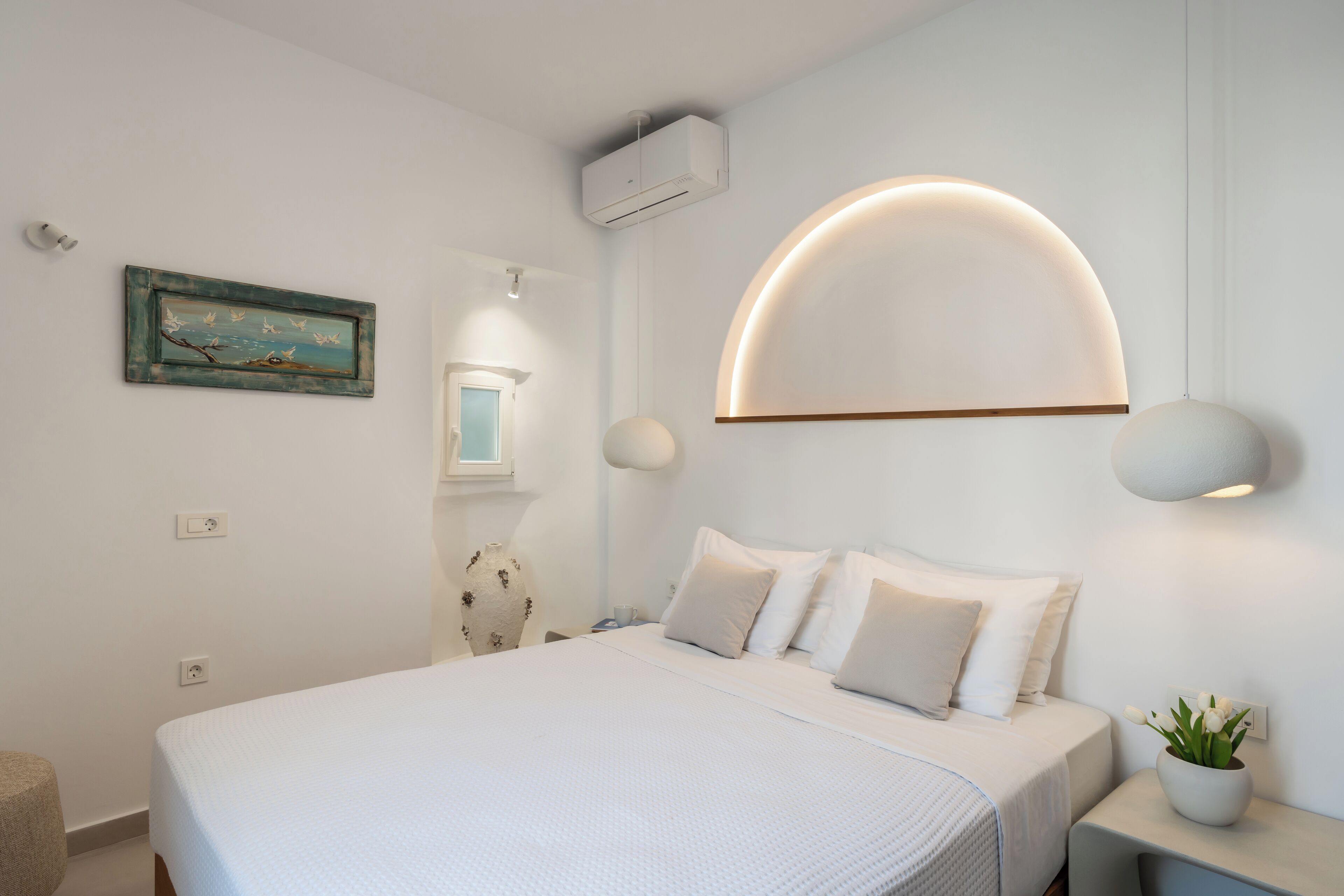 A modern bedroom with a large bed, a wall-mounted air conditioner, a unique ceiling light, and a small potted plant.