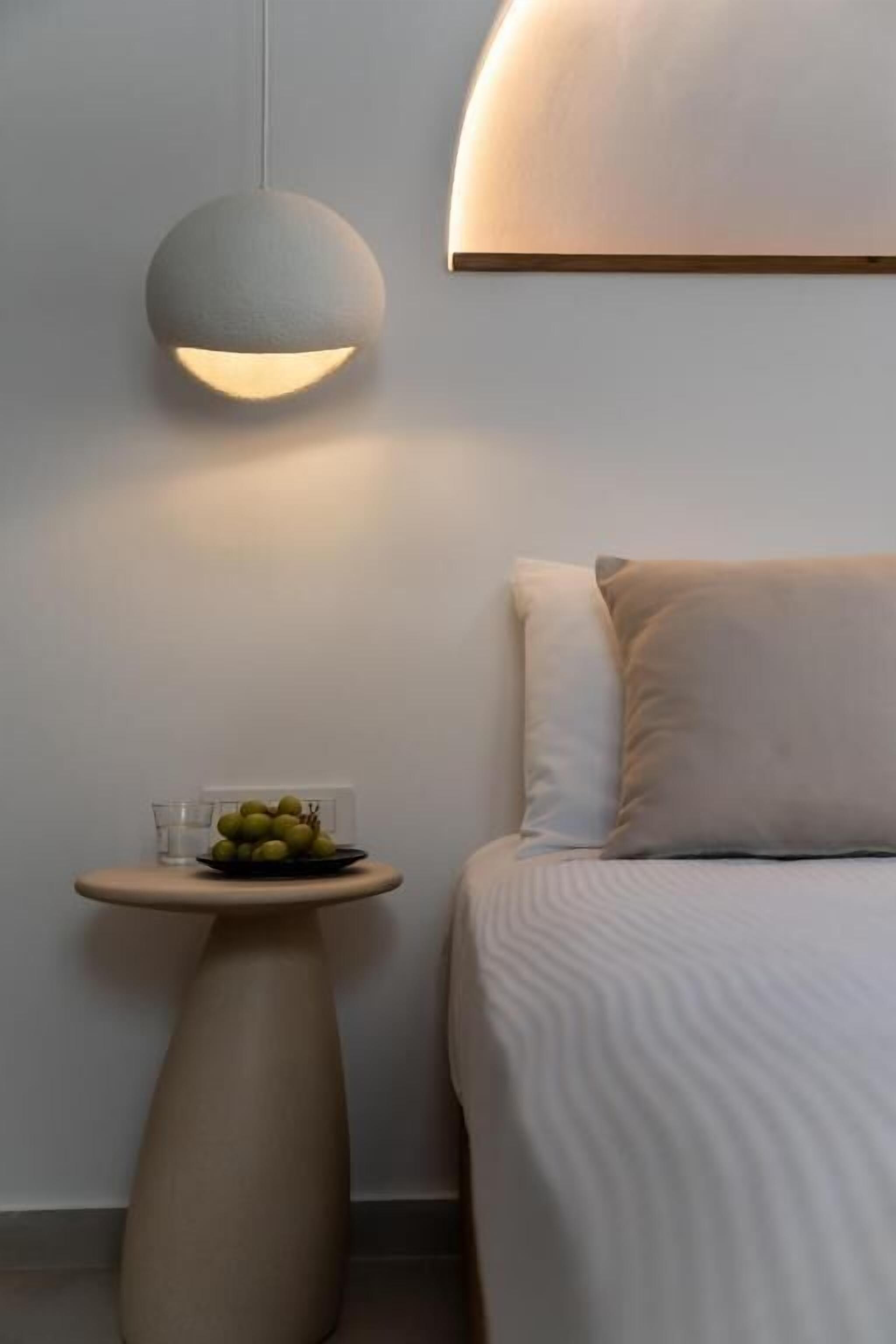 A modern bedroom with a bed, a bedside table with a fruit bowl, and a wall-mounted light fixture.