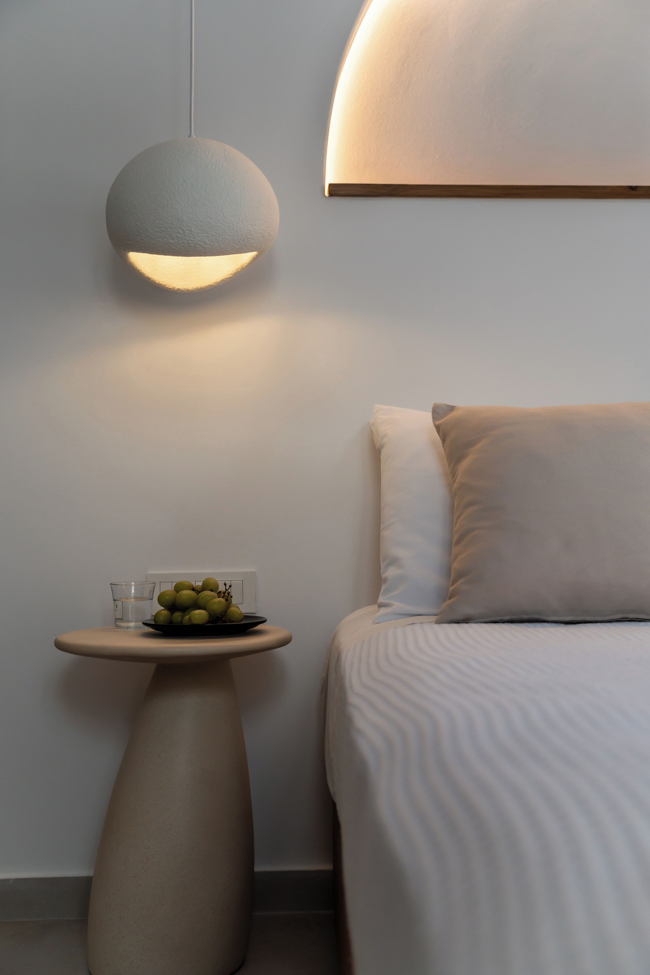 A modern bedroom with a bed, a round table with a plate of fruit, and a wall-mounted lamp.