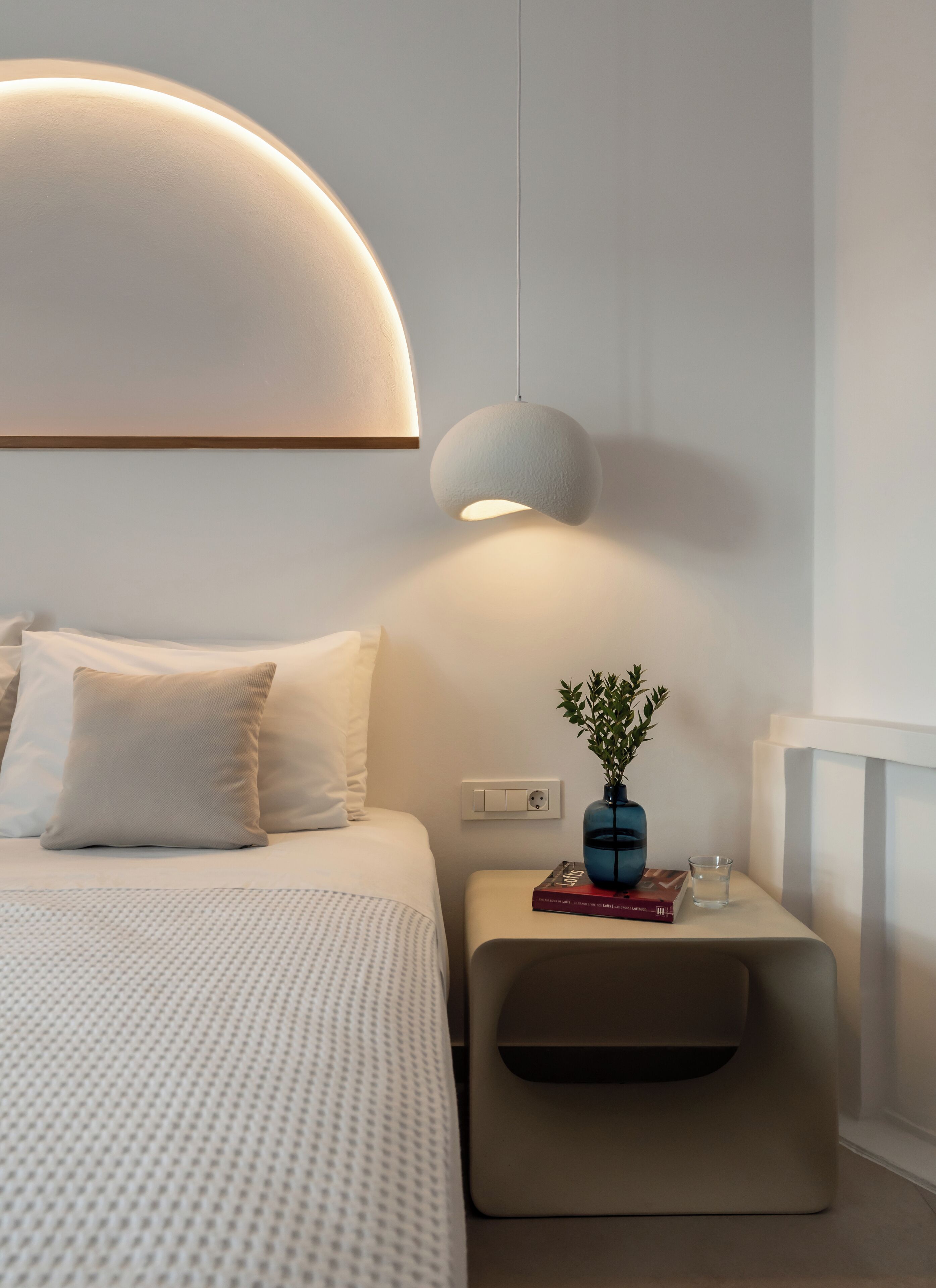 Un dormitorio moderno con cama, mesita de noche y lámpara de pared.