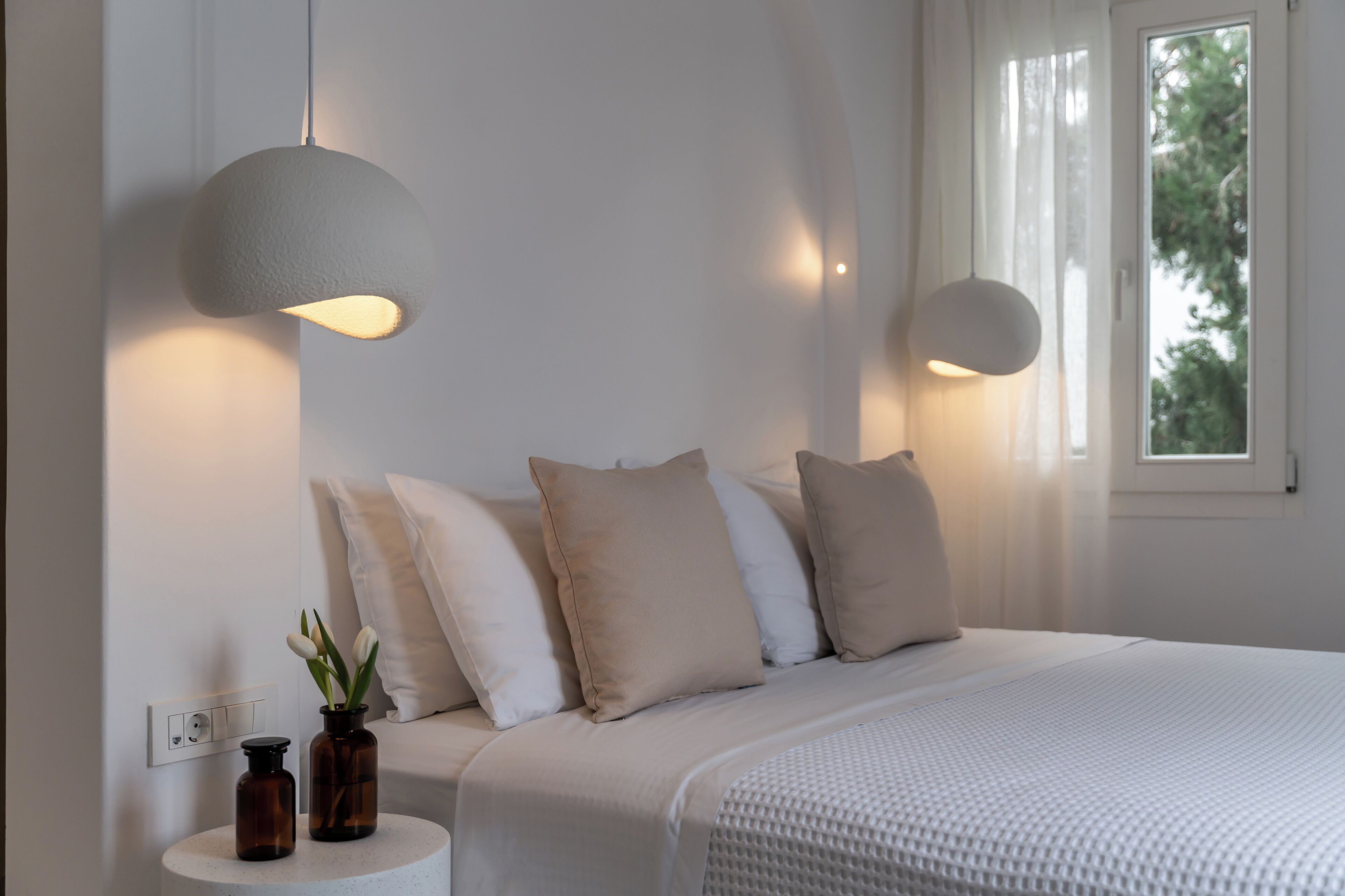 A bedroom with a bed, two bedside tables, a window, and a wall-mounted light fixture.