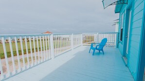 Eine blaue Holzterrasse mit weißer Reling, zwei blaue Stühle und Blick auf den Strand.