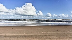 Ein Strand mit an die Küste treibenden Wellen unter einem teils bewölkten Himmel.