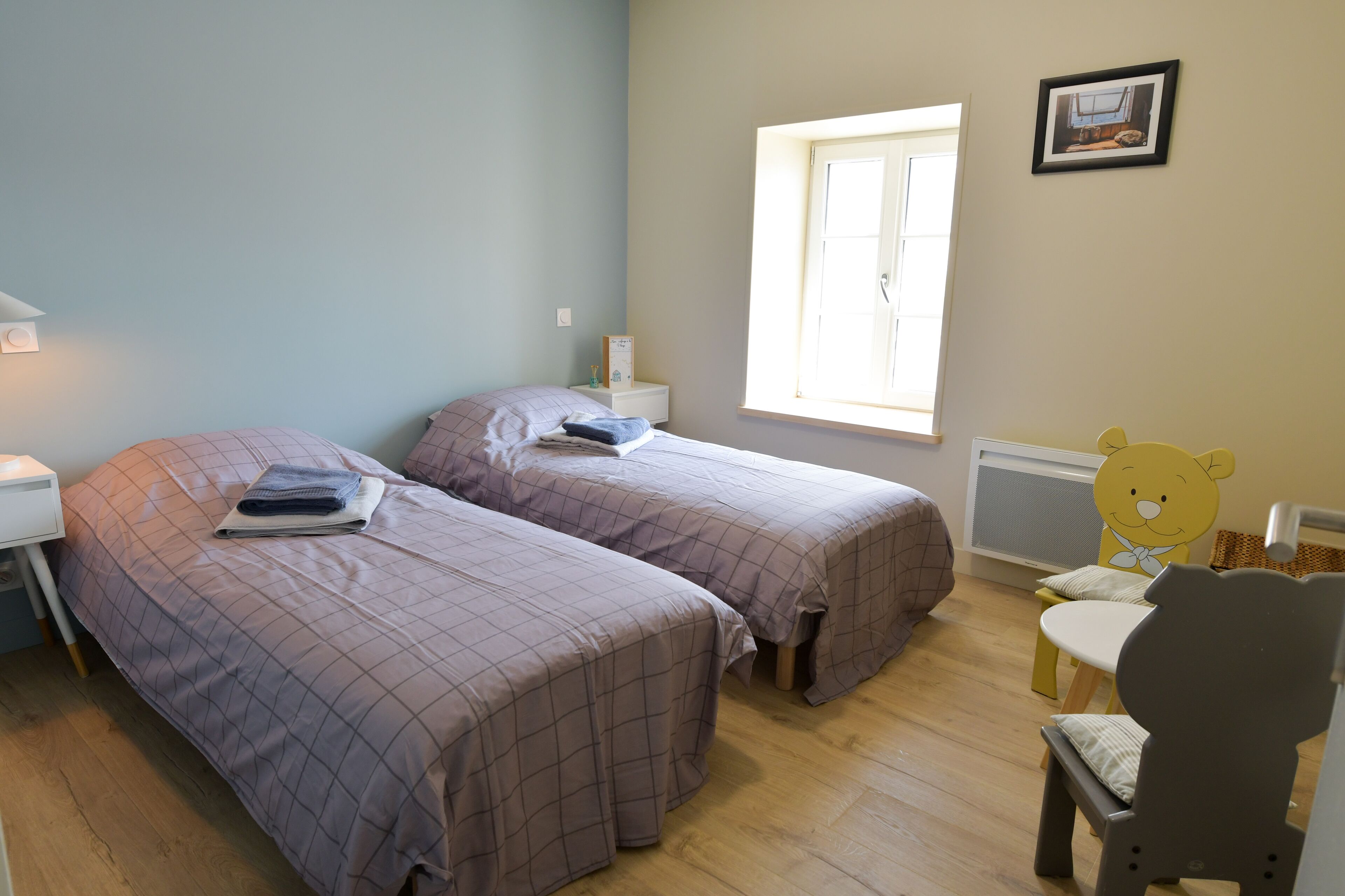 Een slaapkamer met twee bedden, een nachtkastje, een stoel en een raam.