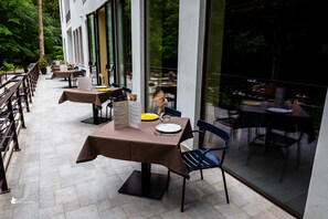 An outdoor dining area with tables and chairs, a potted plant, and a menu stand. - Elda Hotel (Monte Sant'Angelo)