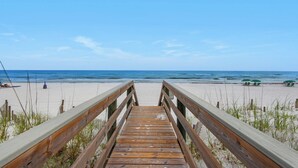 Eine Holzpromenade, die zu einem Strand führt, mit freiem Blick auf das Meer.