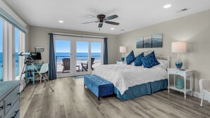 Ein Schlafzimmer mit einem großen Bett, einem Deckenventilator, einem Schreibtisch mit einem Teleskop und Blick auf den Strand durch Glastüren.