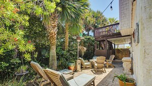 Um terraço ao ar livre com espreguiçadeiras de madeira, uma mesa e plantas em vasos.