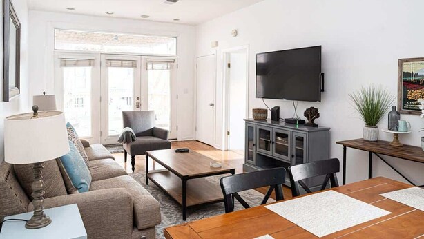 A modern living room with a sofa, coffee table, TV, and dining area. - Urban Oasis - Walk to Restaurants, Transit & More! (Chicago)
