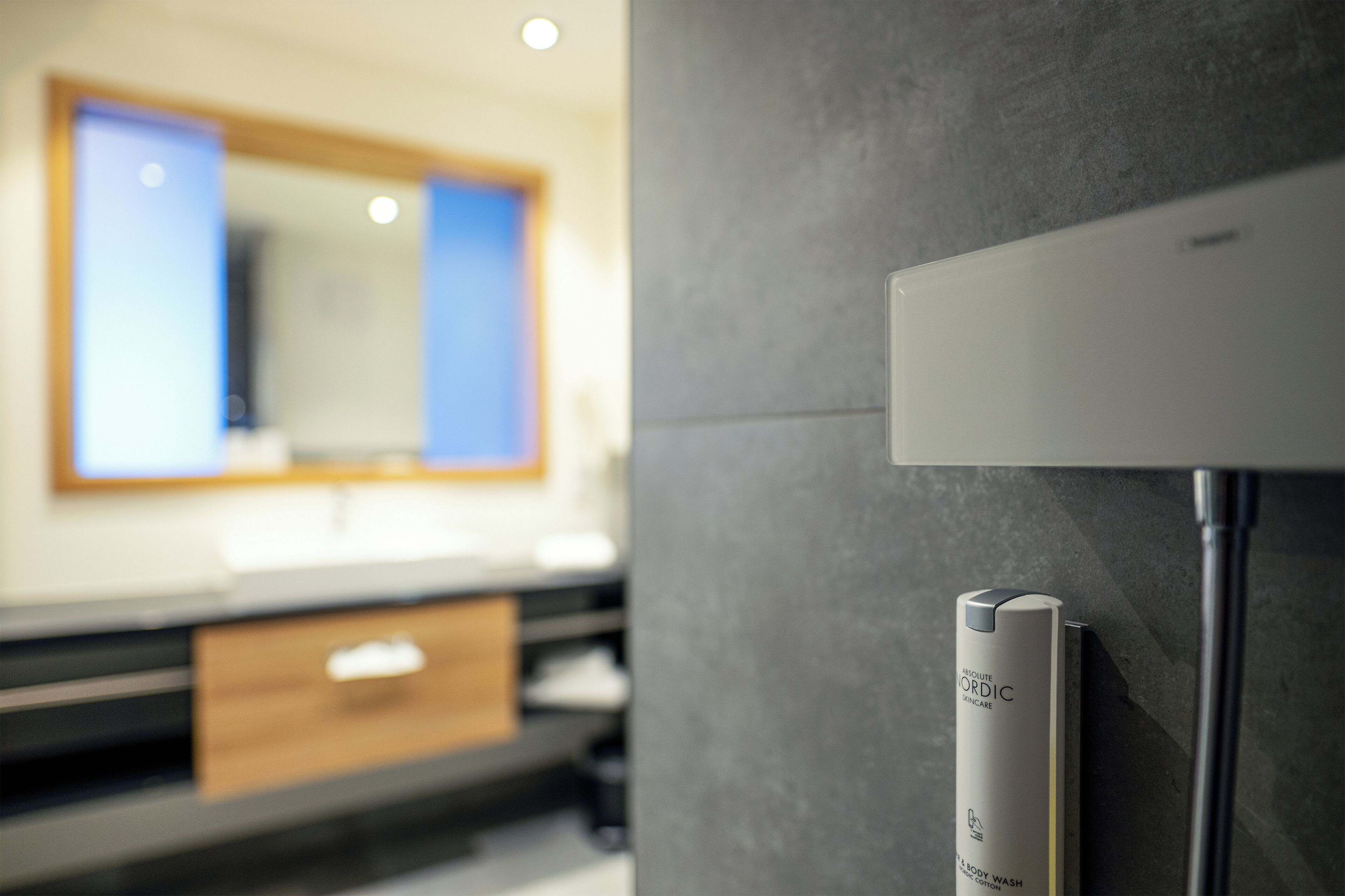 Un baño con diseño moderno, que presenta una pared gris, un espejo y un dispensador de jabón blanco.