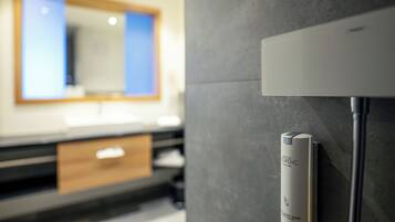 Un baño con diseño moderno, que presenta una pared gris, un espejo y un dispensador de jabón blanco.