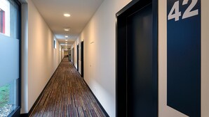 Un largo pasillo estrecho con alfombra estampada, paredes blancas y puertas numeradas 42.