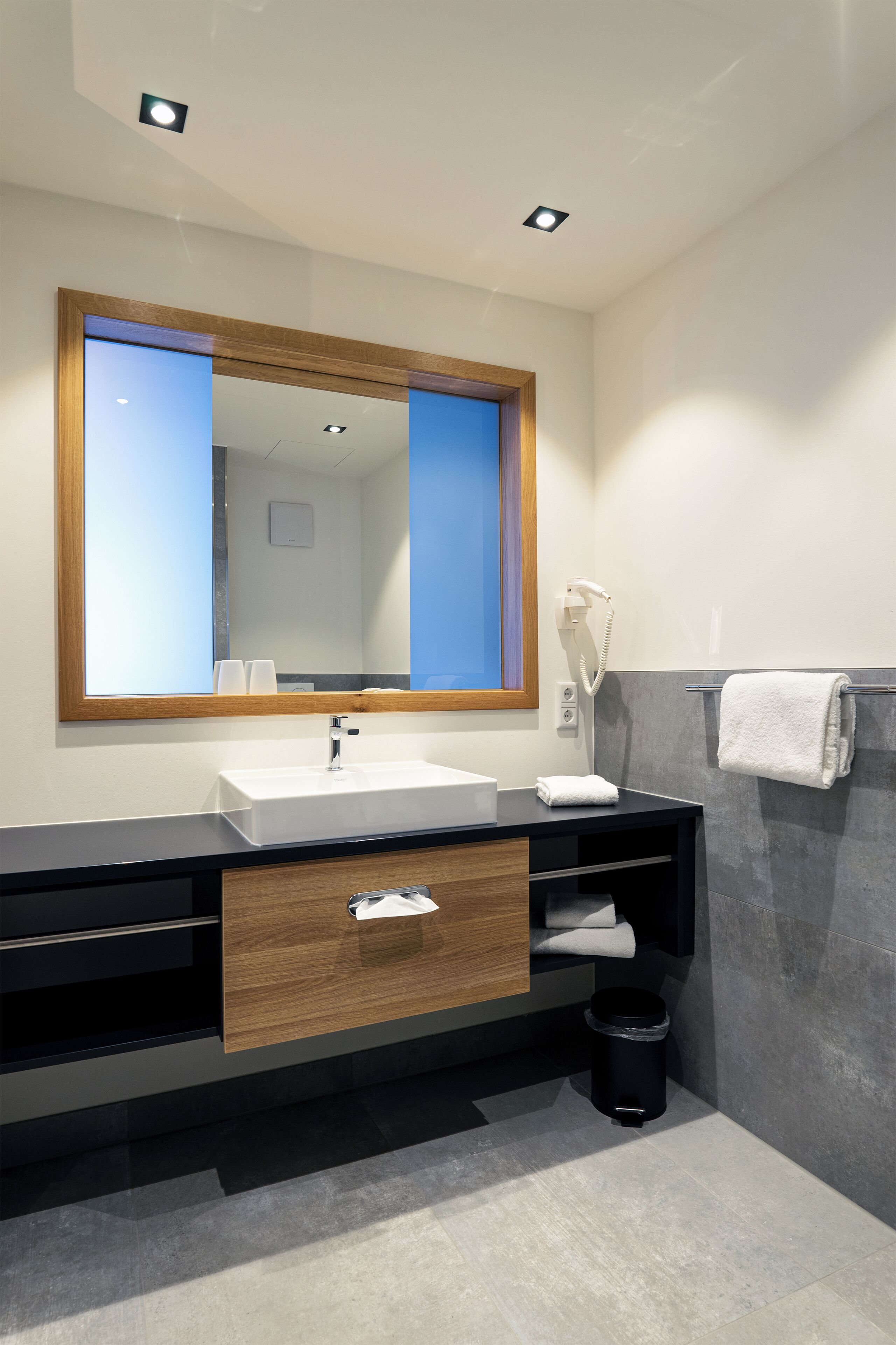 A modern bathroom with a large mirror, white sink, and a towel rack.