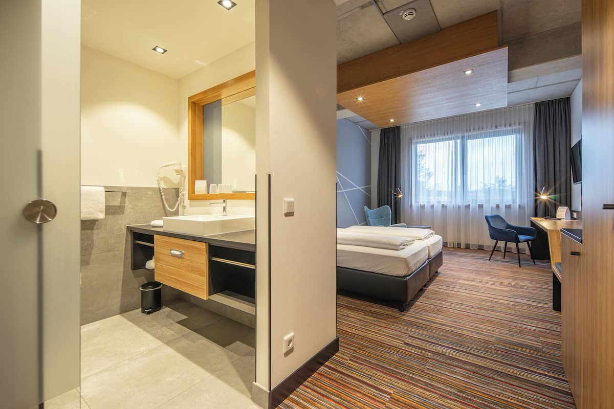 Una habitación de hotel moderna con baño, cama, escritorio y una silla.