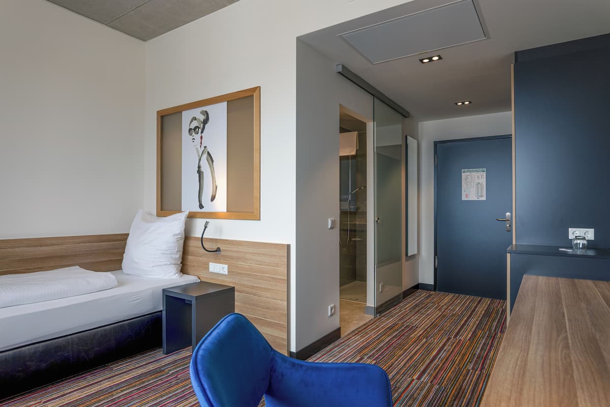 Habitación de hotel con cama, una silla, escritorio y zona de ducha.