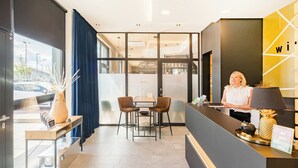 Zona de recepción de hotel con diseño moderno, que incluye un mostrador de recepción, área de estar y ventanas amplias.