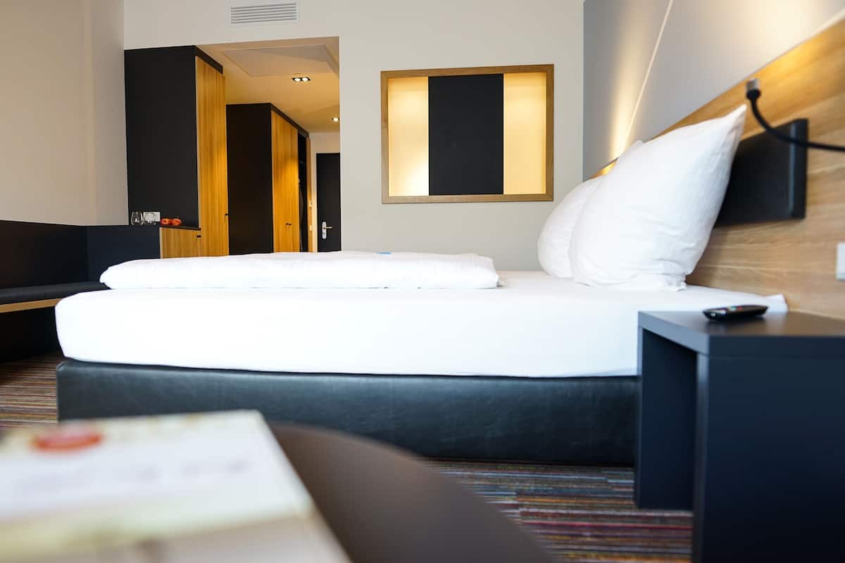 Habitación de hotel con cama, mesita de noche, control remoto y lámpara fijada a la pared.