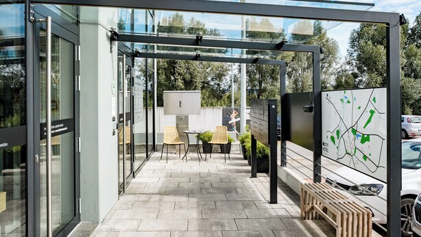 Un área de estar moderna al aire libre con paredes de vidrio, un panel informativo con un mapa y un banco de madera.