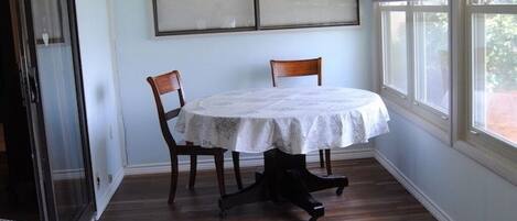 A room with a dining table, chairs, a ceiling fan, a window with blinds, and a wooden floor.