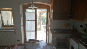 A kitchen with a dining table, chairs, a stove, a washing machine, and a window with curtains. - Two-room apartment with garden and private parking space (Portoferraio)