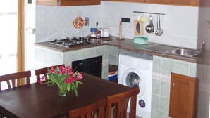 A kitchen with wooden cabinets, a stove, a sink, and a washing machine. - Two-room apartment with garden and private parking space (Portoferraio)