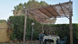 An outdoor patio with a table and chairs, a pergola, and a hedge in the background. - Two-room apartment with garden and private parking space (Portoferraio)