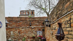 A courtyard with a brick wall, a tiled table, and chairs. There are potted plants and a hanging lantern.