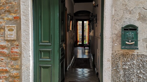 A narrow hallway with a green door, a tiled floor, and a small window with a curtain.