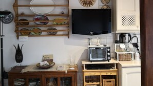 A kitchen with a wooden shelf holding plates, a wall-mounted TV, a Samsung microwave, and a cabinet with a decorative pattern.