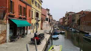 A canal with boats docked, buildings with balconies, and outdoor seating along the water's edge.