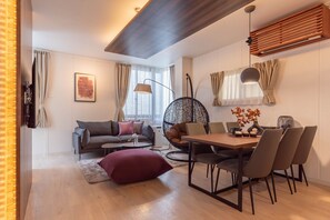 A modern living room with a sofa, a dining table, and chairs. There is a hanging chair and a lamp.
