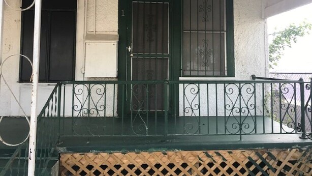 Un porche cubierto con una puerta verde, una ventana con rejas y una barandilla de metal.
