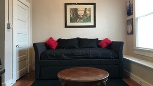 Una sala de estar con un sofá negro, una mesa de centro de madera y un cuadro enmarcado en la pared.