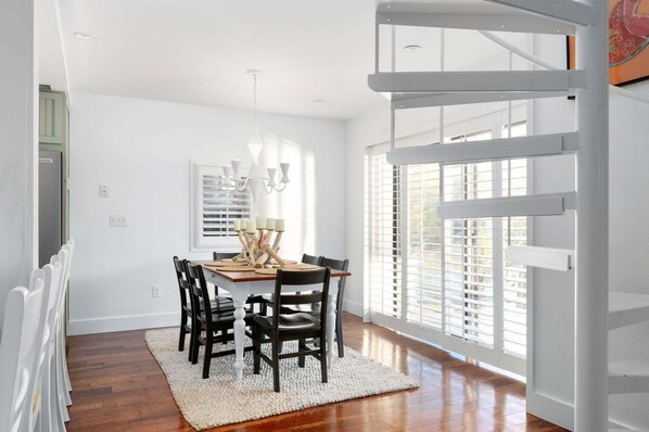 A dining area with a wooden table, black chairs, a white rug, and a chandelier.